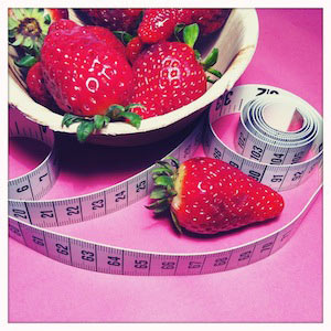 Eine Kartonschale mit Erdbeeren, daneben sieht man ein Maßband.