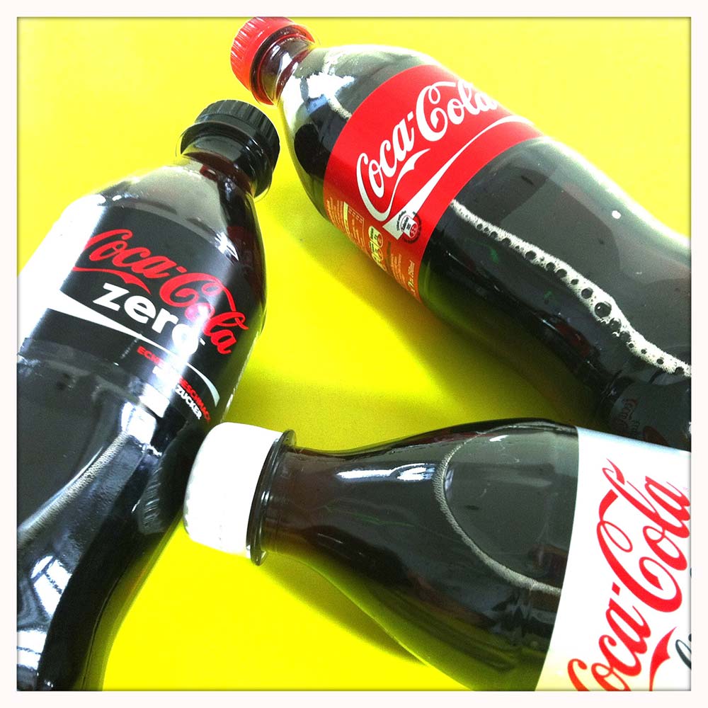 Es gibt Gerüchte, dass Süßstoffe wie Aspartam das Gewicht heben. Dieser Beitrag zeigt auf, wieso das nicht stimmt. Auf dem Beitragsbild sind drei Flaschen Coca-Cola zu sehen.