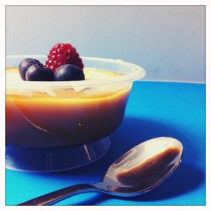 Eine Portion Karamellpudding mit Heidelbeeren und einer Himbeere oben drauf.