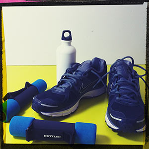 Dunkle Laufschuhe, blaue Hanteln und eine weiße Thermoskanne.