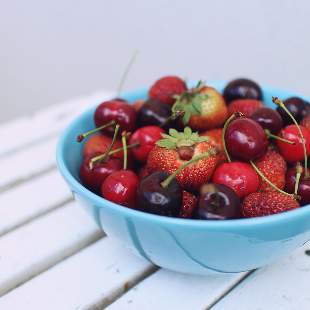 Blaue Schale mit frischen Kirschen und Erdbeeren auf einem weißen Holztisch