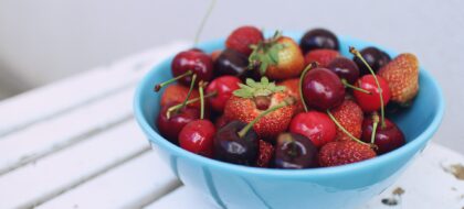 Blaue Schale mit frischen Kirschen und Erdbeeren auf einem weißen Holztisch